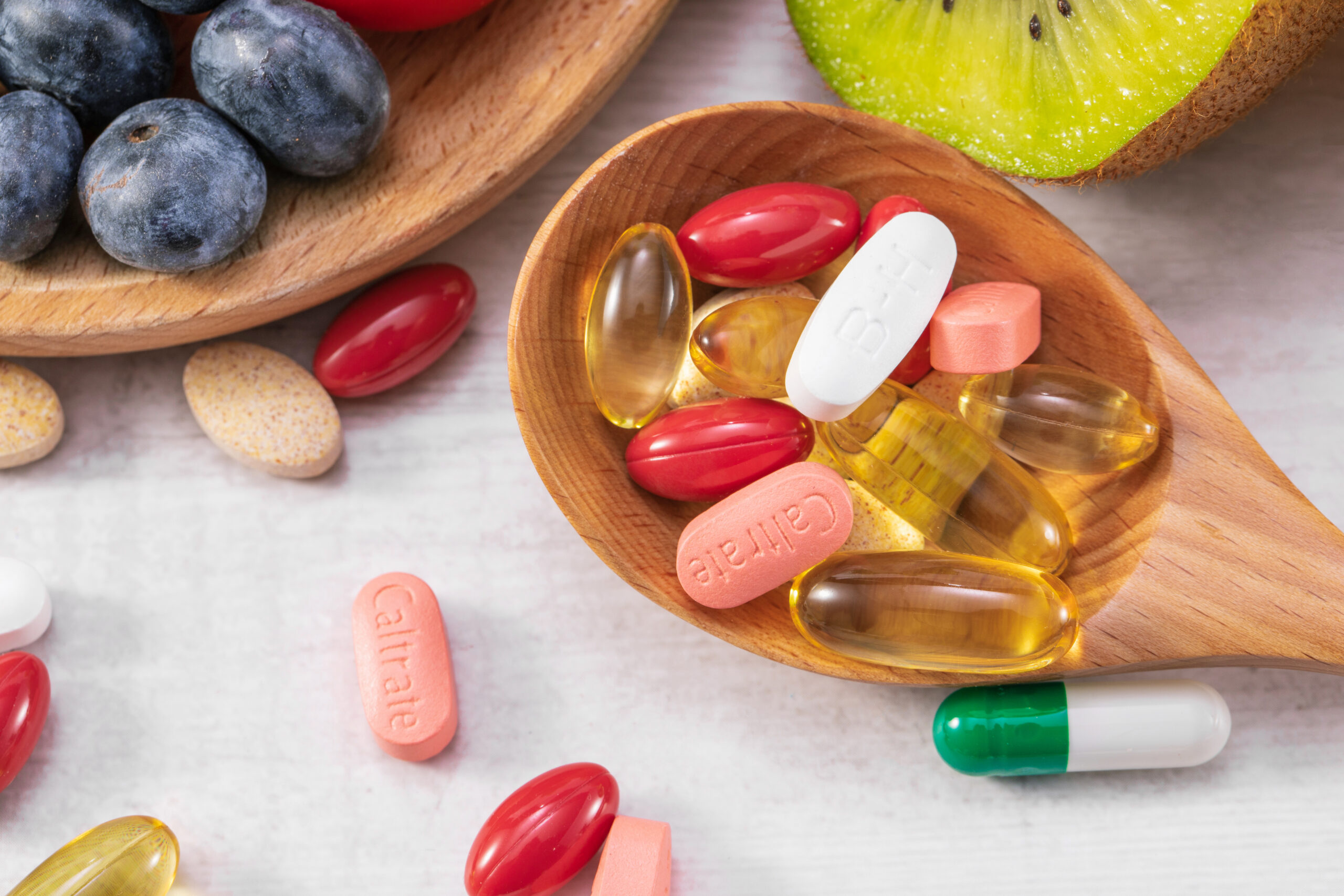 A closeup shot of fresh fruits with different medicine on a wooden spoon